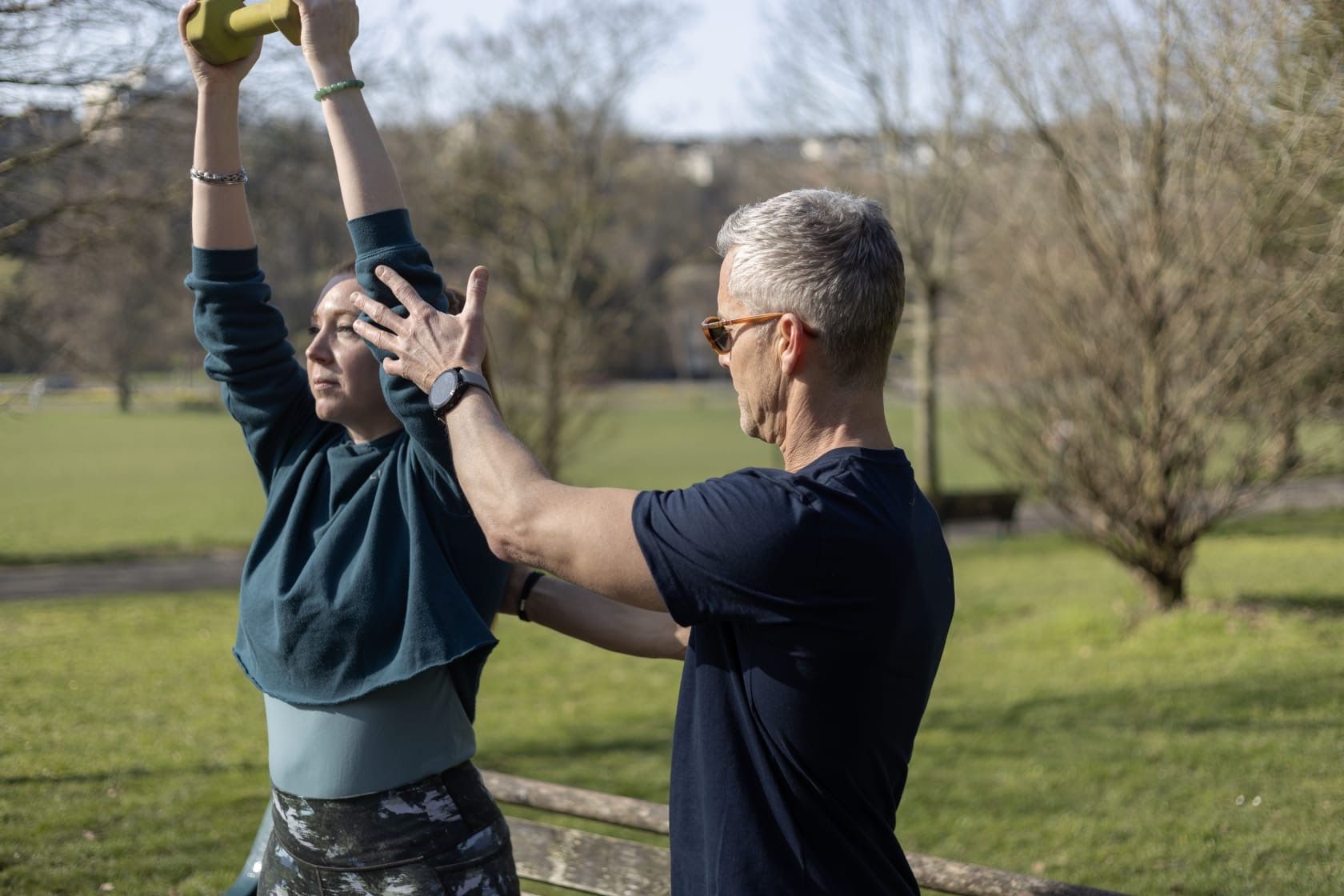 Richard guiding a client through an overhead dumbbell exercise outdoors